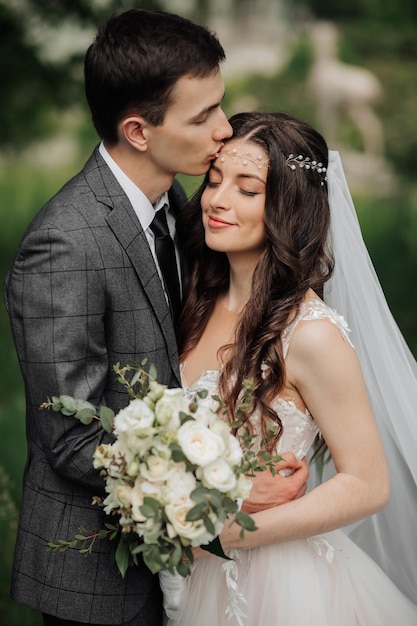 Gelukkige jonge echtpaar Wedding portret De bruidegom kust de bruid op de tempel Jonge mensen knuffelen elkaar teder terwijl ze naar de camera kijken Bruiloftsboeket Lente bruiloft