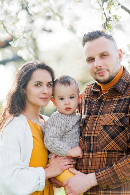 Gelukkige jonge familie brengt tijd door in het voorjaarsbloeiende park moeder vader en kleine zoon spelen buiten