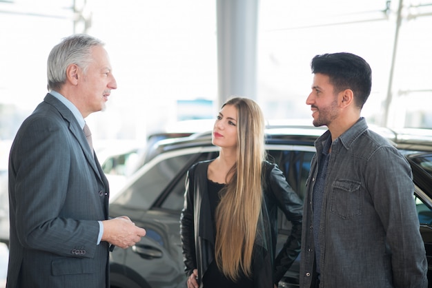 Gelukkige jonge familie die aan de verkoper spreekt en hun nieuwe auto in een toonzaal kiest