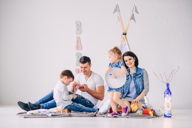 Gelukkige jonge familie die pret in de ruimte van de witte kinderen heeft. Moeder, vader, zus en broer spelen samen.