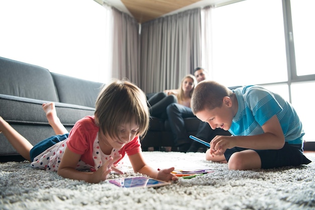 Gelukkige jonge familie die thuis samen op de vloer speelt met een tablet en een tekenset voor kinderen