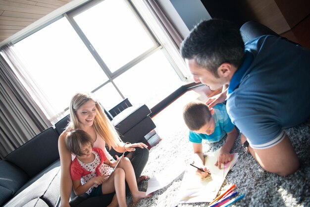 Gelukkige jonge familie speelt thuis samen op de vloer met behulp van een tablet en een tekenset voor kinderen