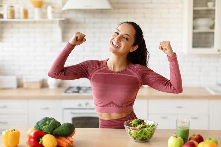 Foto gelukkige jonge fitnessdame die bicepsspieren toont terwijl ze binnenshuis kookt