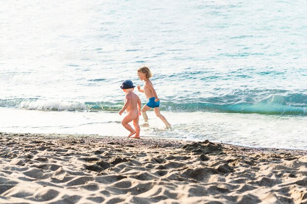 Gelukkige jonge geitjes op vakantie aan zee lopen in het water jongen en meisje spelen op het strand in de zomer ...