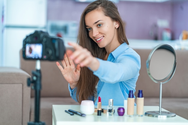 Gelukkige jonge glimlachende vrouw video blogger tijdens het opnemen van haar schoonheid vlog over make-up en cosmetica thuis. Bloggen en live streamen