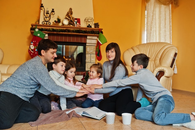 Gelukkige jonge grote familie thuis bij een open haard in warme woonkamer op winterdag hand op handen