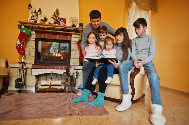 Gelukkige jonge grote familie thuis bij een open haard in warme woonkamer op winterdag.
