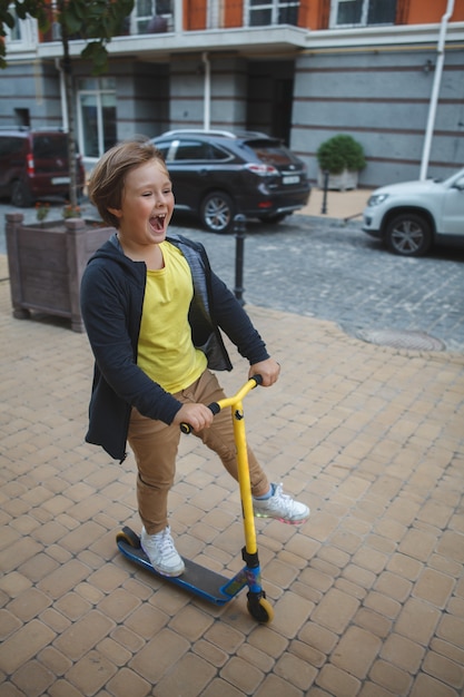 Gelukkige jonge jongen die van het berijden van een autoped op stadsstraten geniet