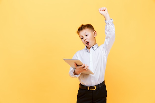 Gelukkige jonge jongen in formele kleding die tablet gebruiken. Studioschot op geel wordt geïsoleerd dat. Winnaar.