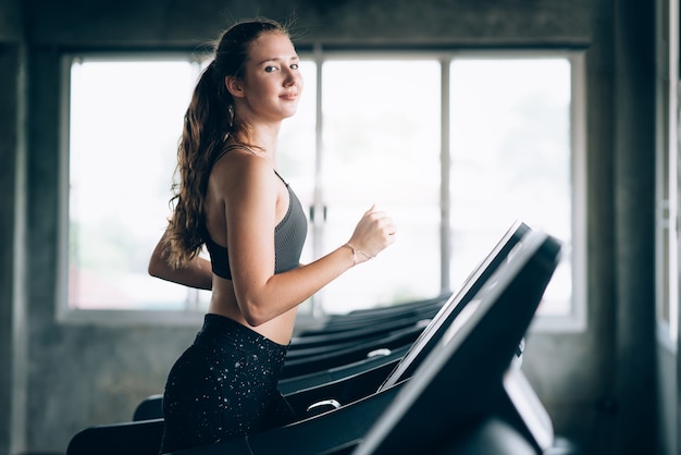 Gelukkige jonge Kaukasische vrouw die cardio doen door op tredmolen in gymnastiek in werking te stellen