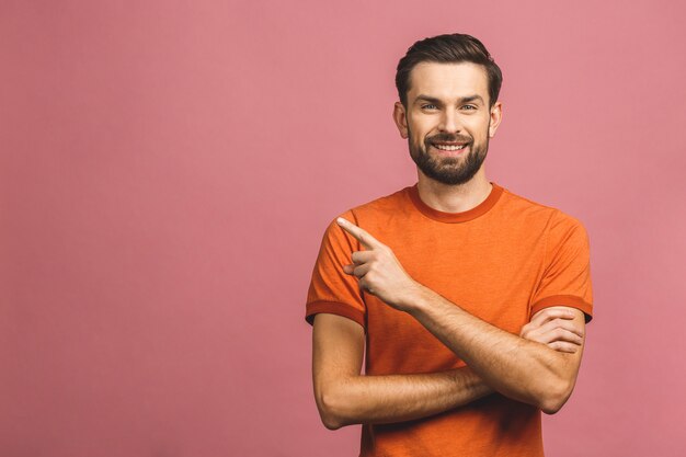 Gelukkige jonge knappe mens in weg en toevallig het richten terwijl status tegen roze muur glimlachen.