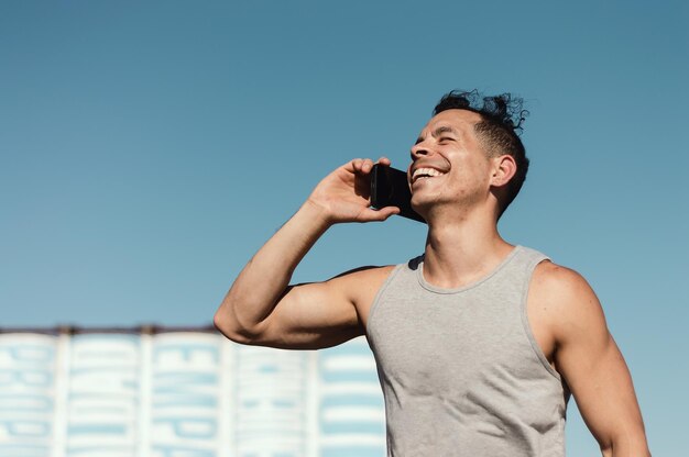 Gelukkige jonge latijns-kaukasische man buiten glimlachend en pratend aan de telefoon