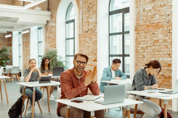 Gelukkige jonge man aan het werk met laptop in de klas