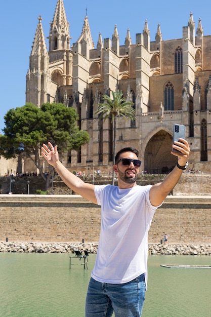 Gelukkige jonge man die een foto maakt met zijn mobiele telefoon in de kathedraal van Palma de Mallorca in Spanje