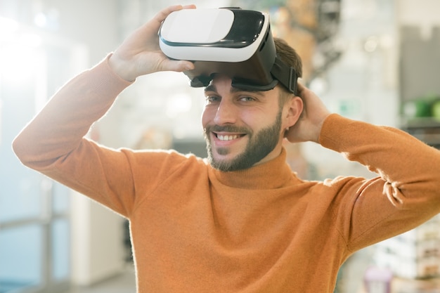 Gelukkige jonge man die je met een glimlach bekijkt terwijl hij de vr-headset opstijgt na het bekijken van virtueel assortiment