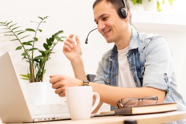 Gelukkige jonge man die lacht, terwijl hij op zijn laptop werkt om al zijn zaken 's ochtends vroeg af te handelen met zijn kopje koffie