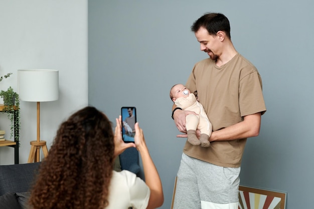 Gelukkige jonge man die naar de baby op zijn handen kijkt terwijl een vrouw er een foto van maakt