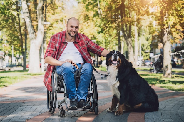 Gelukkige jonge man met een lichamelijke handicap die rolstoel gebruikt met zijn hond