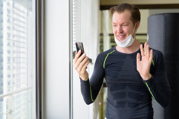 Gelukkige jonge man met masker videogesprek en klaar om te trainen tijdens covid-19