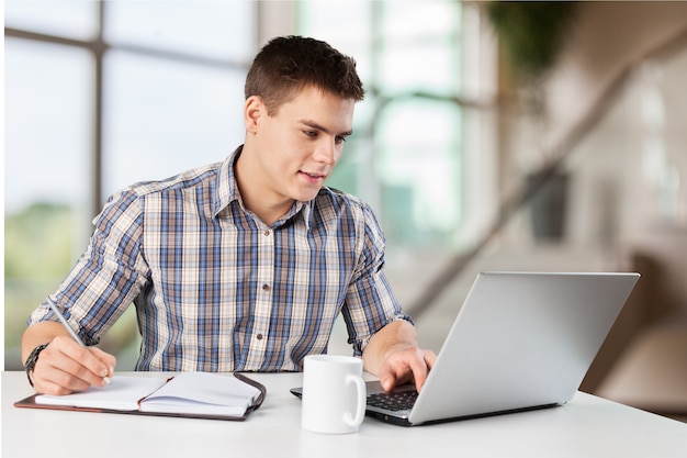 Gelukkige jonge man werkt op zijn laptop met koffie aan tafel