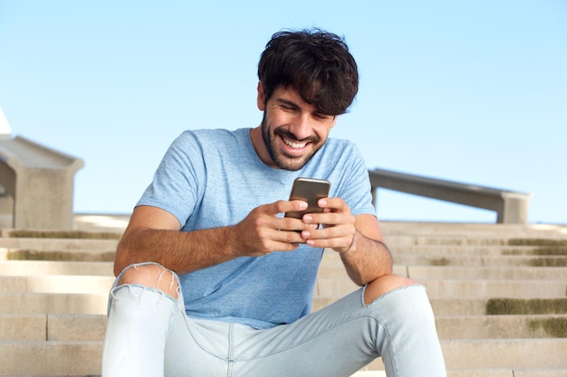 Gelukkige jonge man zit met een mobiele telefoon