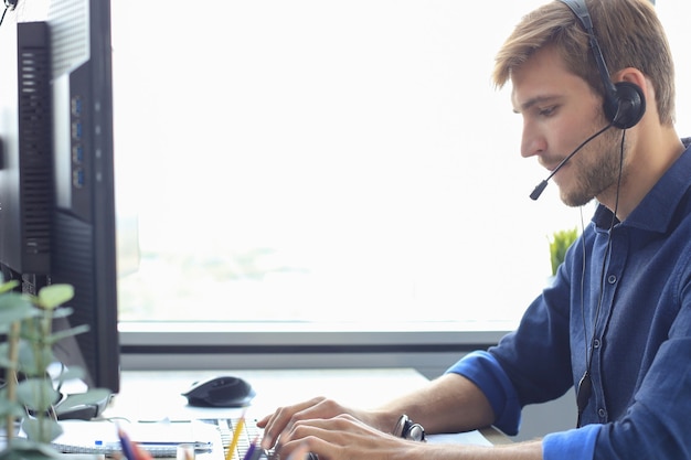 Gelukkige jonge mannelijke klantenservicemedewerker die op kantoor werkt.