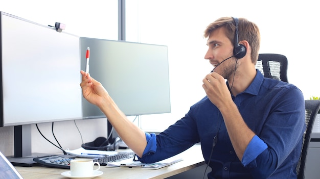 Gelukkige jonge mannelijke klantenservicemedewerker die op kantoor werkt.