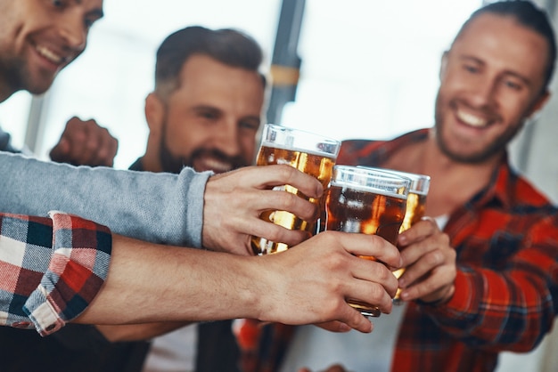 Foto gelukkige jonge mannen in vrijetijdskleding die elkaar roosteren met bier en glimlachen