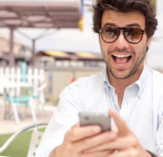 Gelukkige jonge mens die een mobiele telefoon met behulp van