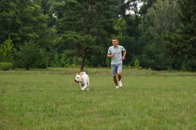 Gelukkige jonge mens die met hond Labrador in openlucht loopt