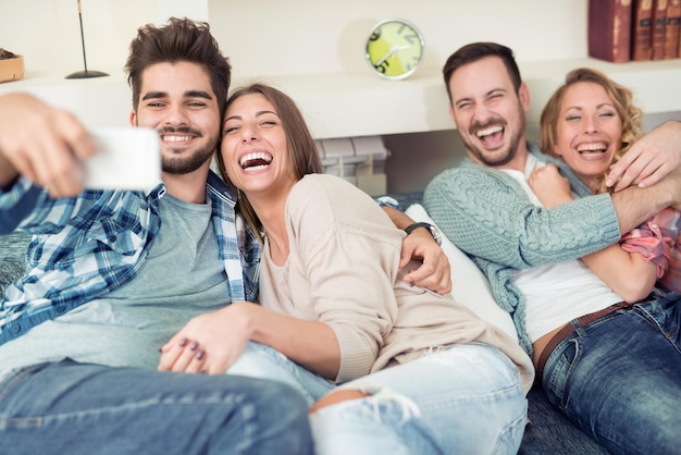 Gelukkige jonge mensen genieten van tijd samen zittend op de bank thuis, selfie te nemen.