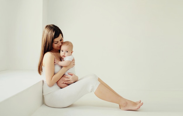 Gelukkige jonge moeder die een schattige baby vasthoudt in een witte kamer thuis