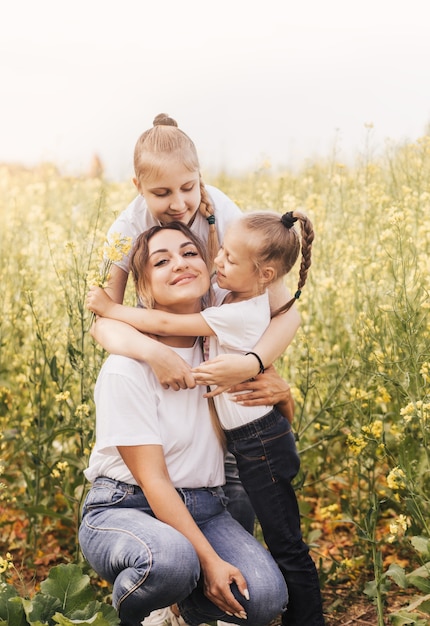 Gelukkige jonge moeder knuffelt met haar dochters in de zomer op het gebied van verkrachting. Geluk met familie
