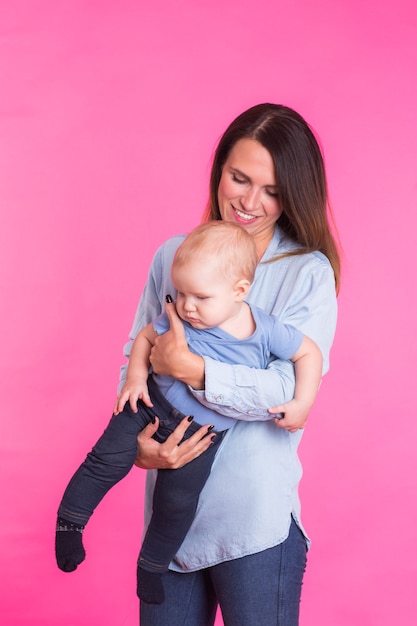 Gelukkige jonge moeder met een babykind op roze muur.