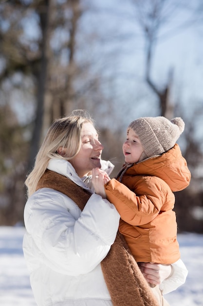 Gelukkige jonge moeder met zoon lopen in het winterpark Portret gelukkig gezin buiten Jongen gooit sneeuw in moeder