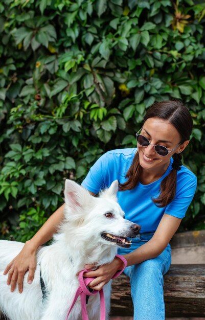 Gelukkige jonge mooie brunette meisje omhelst haar schattige witte pluizige hond buiten in het park op het gazon Adoptie gered schuilplaats metgezel huisdier