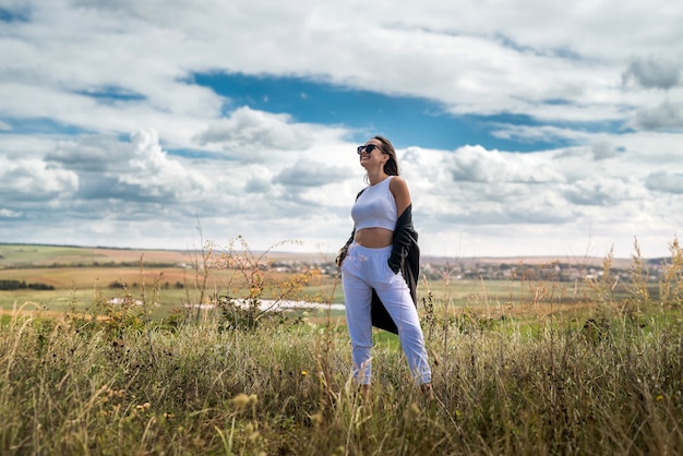 Gelukkige jonge mooie vrouw genieten van het landschap in de buurt van groen veld in de zomer