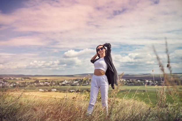 Gelukkige jonge mooie vrouw genieten van het landschap in de buurt van groen veld in de zomer