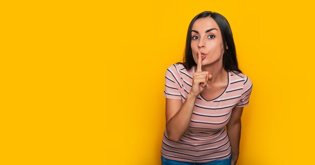 Gelukkige jonge mooie vrouw in een t-shirt, die in de camera kijkt en een stil gebaar toont met haar wijsvinger