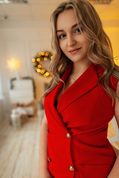 Gelukkige jonge mooie vrouw met kapsel in mode rode blazer op achtergrond van kerstversiering thuis