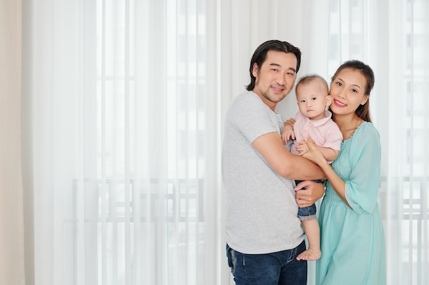 Gelukkige jonge ouders houden hun ernstige zoontje en kijken naar camera