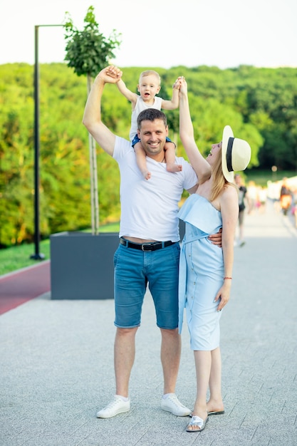 Gelukkige jonge ouders, mama en papa lopen met een baby in een kinderwagen in het park in een hoed in de zomer in de ondergaande zon en lachend met plezier