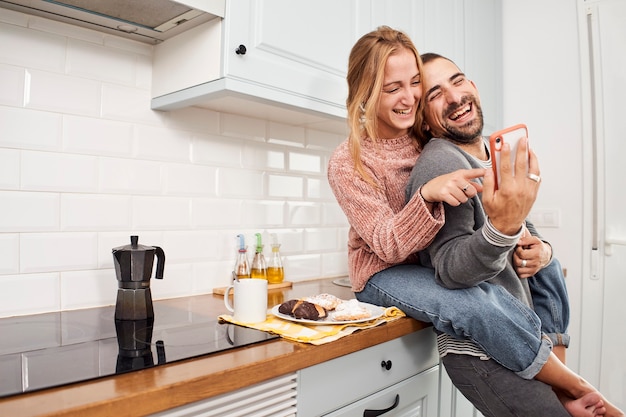 Gelukkige jonge paar in keuken thuis, met behulp van mobiele telefoon en lachen