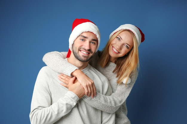 Gelukkige jonge paar in Santa hoeden op kleur achtergrond. Kerst concept