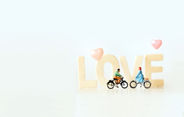 Gelukkige jonge paarminiatuur op fietstocht met "LIEFDE" tekst. Valentijnsdag met vintage kleurenthema.