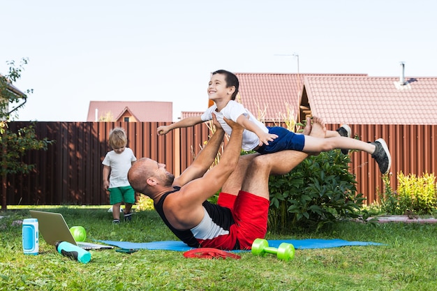 Gelukkige jonge papa speelt met haar baby op een groen gazon. Concept van een gelukkig gezin. Vaderdag. Vader en zoon hebben samen activiteiten op vakantie in de achtertuin