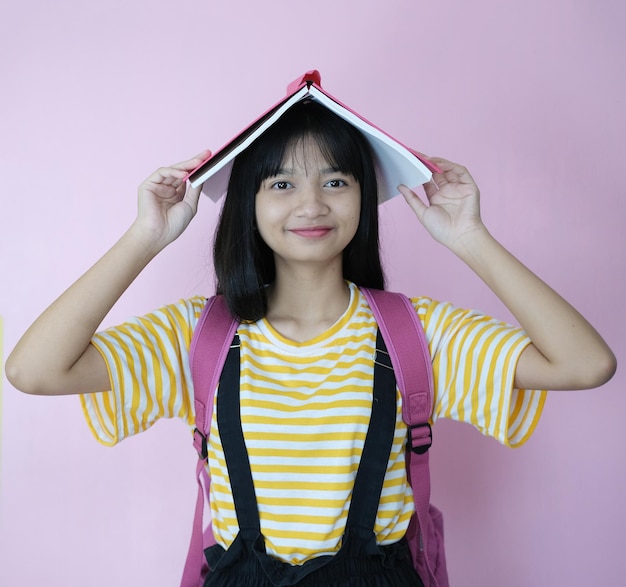 Gelukkige jonge student die roze boek met rugzak op roze achtergrond houdt.