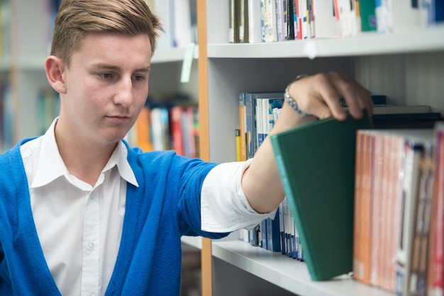 Gelukkige jonge studenten die in universiteitsbibliotheek bestuderen die een boek van plank plukken