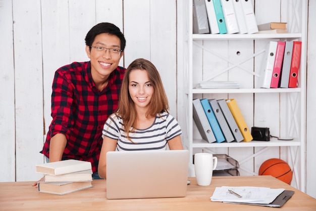 Gelukkige jonge studenten kijken naar voren en werken met laptop en boeken.