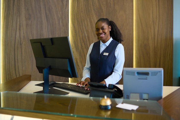 Gelukkige jonge succesvolle vrouwelijke receptioniste in uniform bij de balie